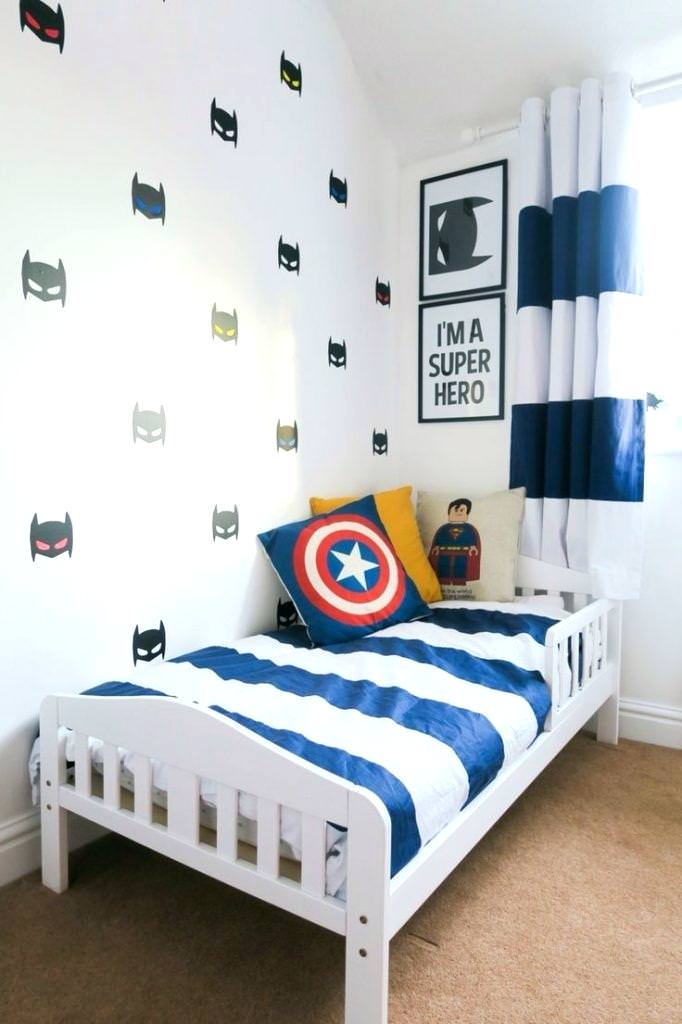 دکوراسیون اتاق کودک پسرانه ای با تخت سفید چوبی که روبالشی، تابلو و استیکرهای دیواری به طرح بتمن و سوپرمن دارد